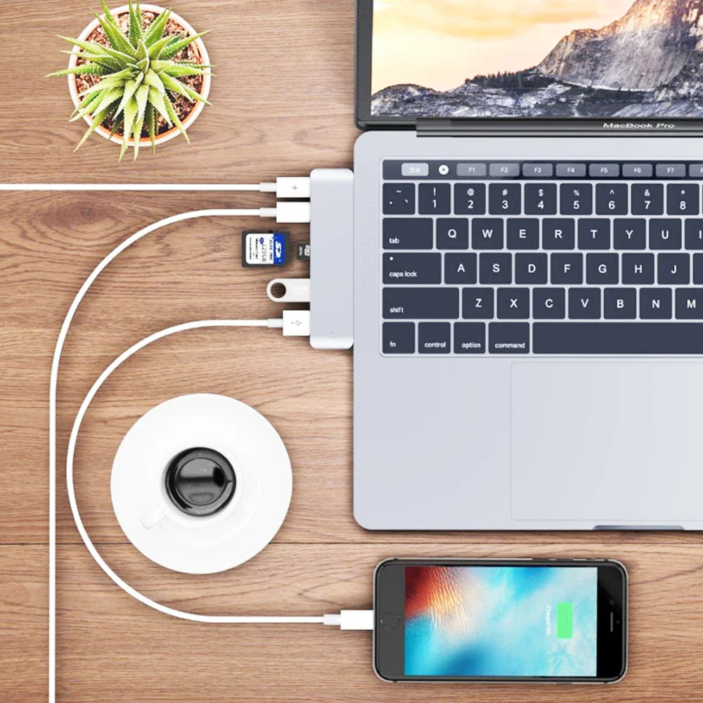 USB C Hub for MacBook Pro Adapter in use on a wooden desk setup. Multiple devices connected including phone, SD card, and USB drive.