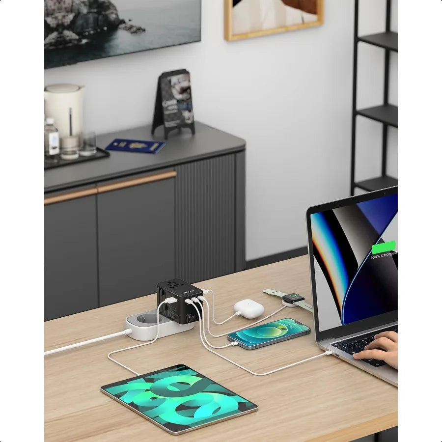 Compact universal travel adapter with multiple USB ports charging laptop, tablet, and smartphone on desk