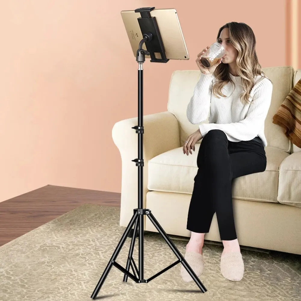 Adjustable tripod floor tablet stand with carbon steel material holding a tablet beside woman sitting on sofa drinking beverage