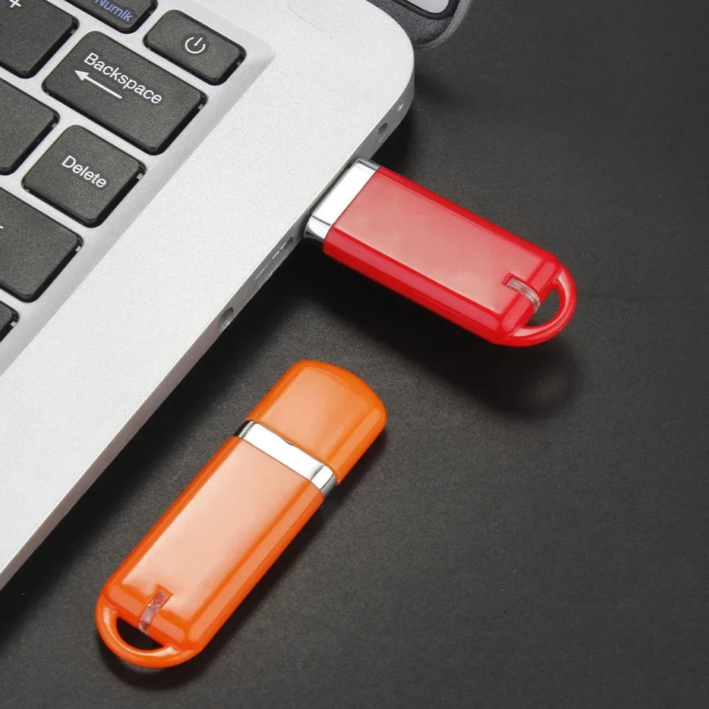 Red and orange JASTER 64GB USB Flash Drives plugged into a laptop, showcasing USB 2.0 connectivity for business use.